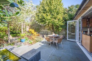 Een terras buiten met een ronde tafel en stoelen, omgeven door een stenen vloer en een fonteintje.