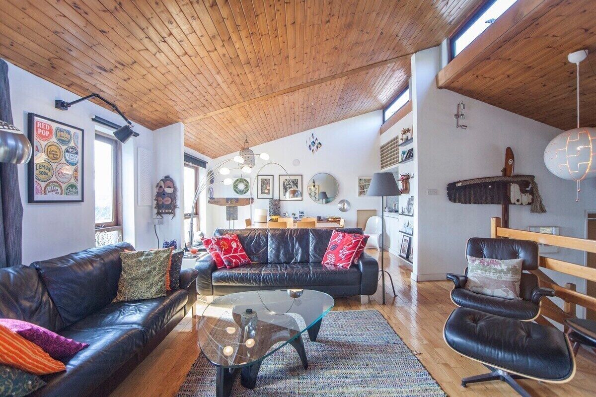 Un salon moderne avec un plafond en bois, des canapés en cuir, une table basse en verre et un plancher en bois.
