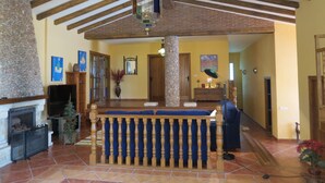 Amplia sala de estar con techo alto, vigas de madera a la vista, un pilar de piedra, chimenea y un banco acolchado azul.