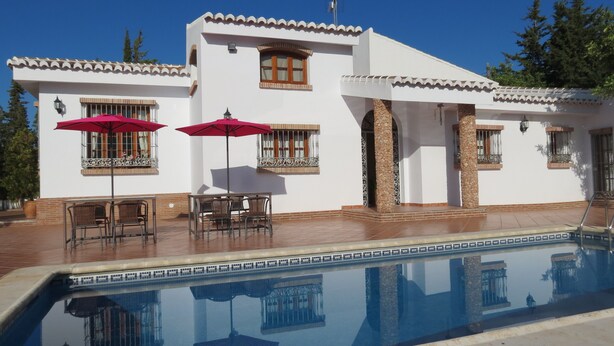 Un edificio blanco con piscina, mobiliario exterior y pilares de piedra.