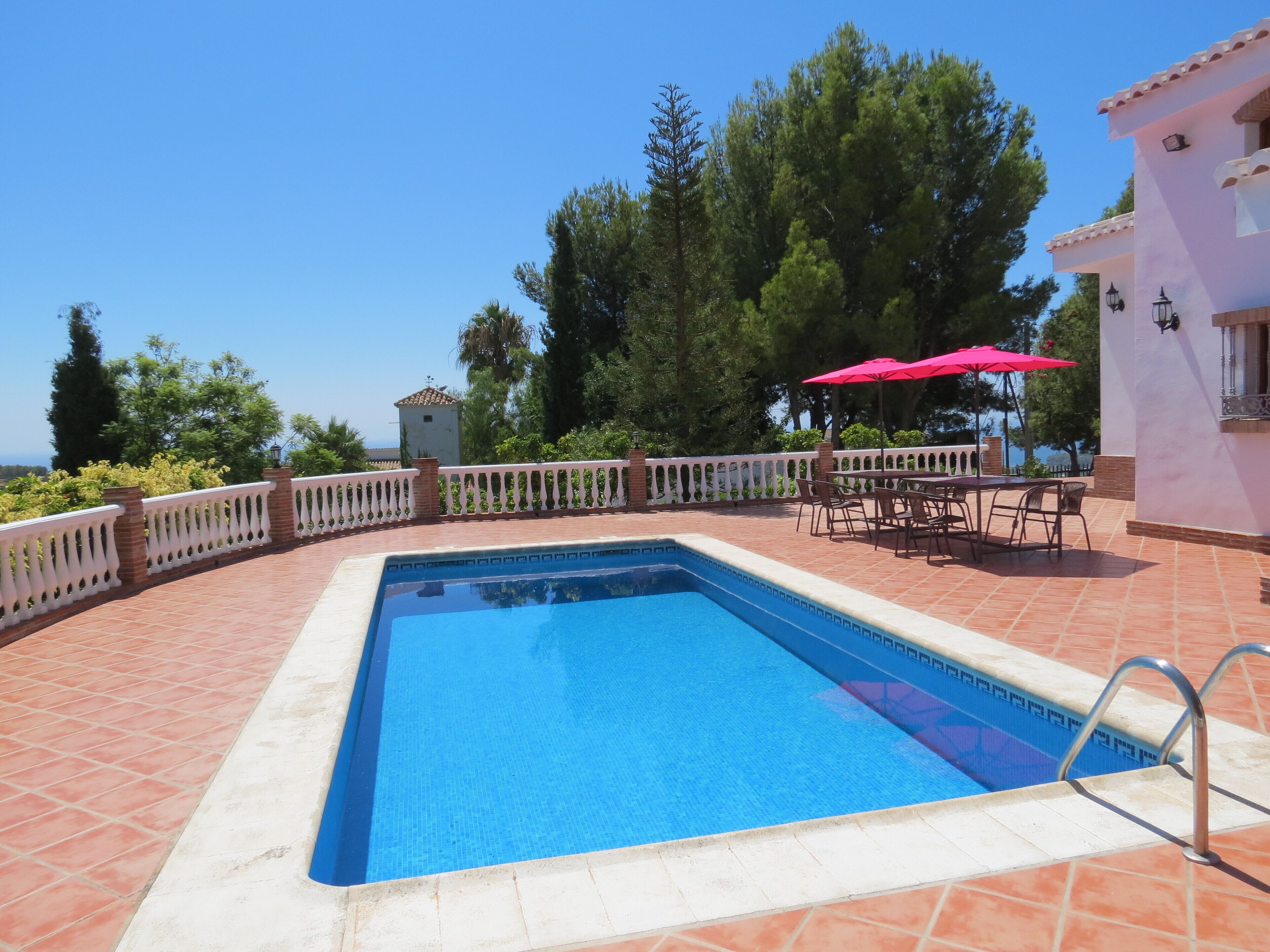 Una piscina rectangular con borde blanco, rodeada por una cerca blanca y una zona de patio con baldosas.