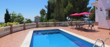 Una piscina rectangular con borde blanco, rodeada por una cerca blanca y una zona de patio con baldosas.