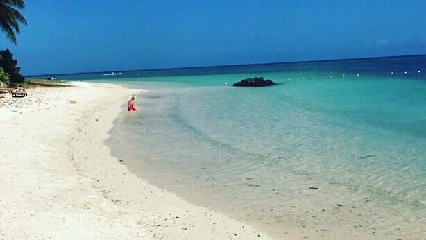Una playa con agua turquesa cristalina, una orilla de arena y algunas personas.