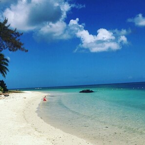 Une plage à l’eau turquoise et limpide, un rivage sablonneux et quelques personnes.