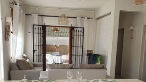 Una sala de estar moderna con un sofá, una mesa de comedor con una bandeja y vasos, y vistas a un área exterior con mesas y sillas.