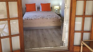 Una habitación con una cama, dos almohadas naranjas, una mesita de noche con lámpara y un ventilador de techo.