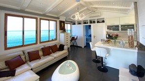 Een moderne woonkamer met een bank, een glazen salontafel en uitzicht op de oceaan door grote ramen.