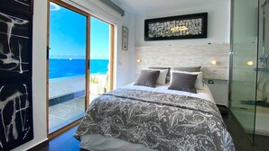 Een slaapkamer met een groot bed, uitzicht op zee, een glazen douche en een moderne plafondlamp.