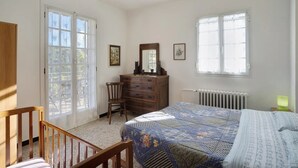Een slaapkamer met een bed, een dressoir, een stoel en twee ramen.