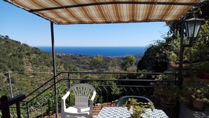 Een terras met een tafel en stoelen, met uitzicht op een schilderachtig zee- en heuvellandschap.