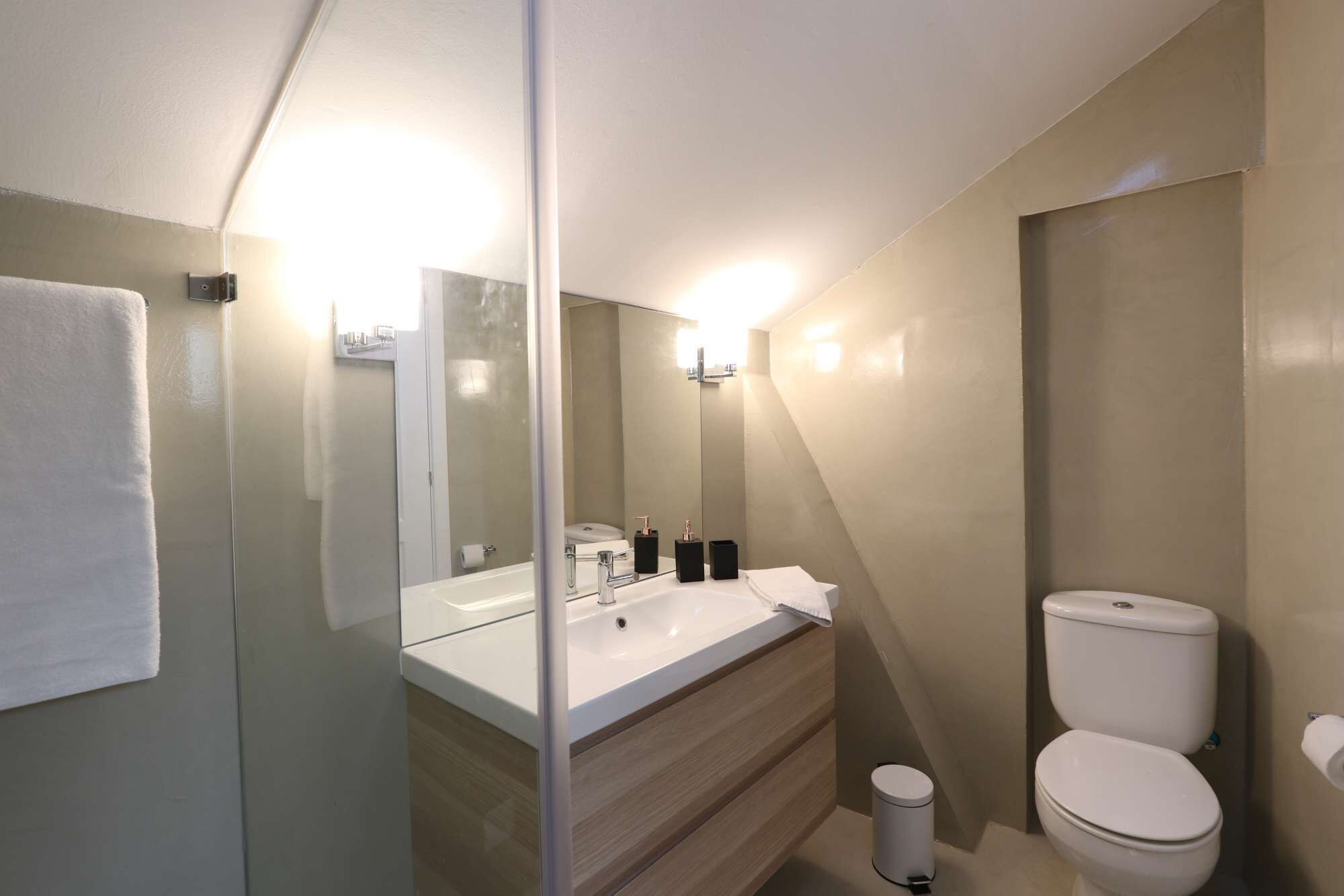 Un baño moderno con cabina de ducha de vidrio, un lavabo blanco con espejo y un inodoro.