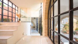 Un intérieur moderne avec un escalier menant à un deuxième étage, de grandes fenêtres et une vue sur une cour extérieure agrémentée de plantes en pot.