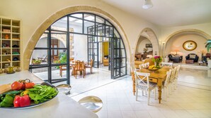 Un vaste espace de vie comprenant un coin repas avec une table et des chaises, ainsi qu’une cuisine équipée avec un panier de fruits et des légumes.