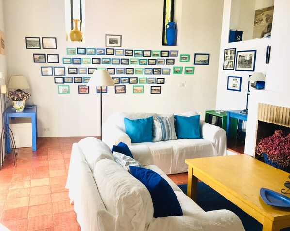 A living room with a white sofa set, a blue and white striped throw pillow, a yellow coffee table, and a wall decorated with numerous framed photographs.
