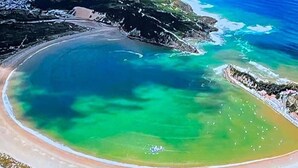 An aerial view of a coastal area with a beach, clear waters, and rocky outcrops.