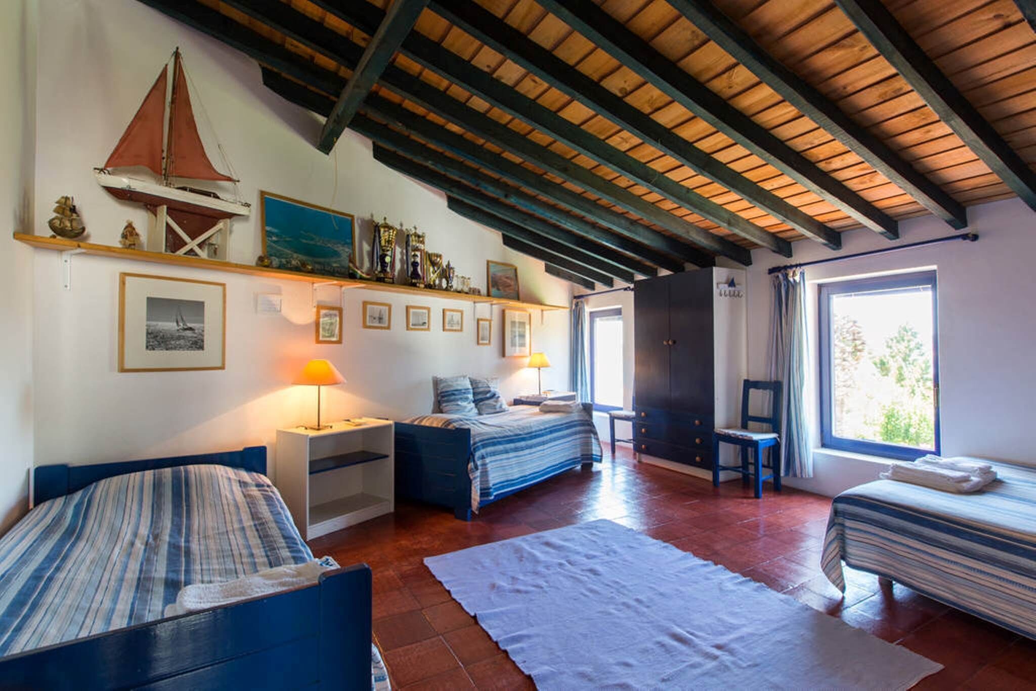 Een kamer met een houten plafond, een bed, een bureau, een stoel en een raam.