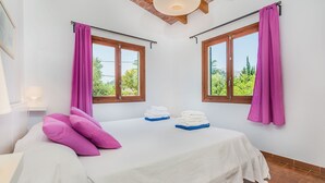 Een slaapkamer met twee ramen, een bed met wit beddengoed, roze kussens en handdoeken op de vensterbank.