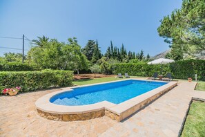 Una piscina rectangular con borde de piedra, rodeada por un patio de piedra.