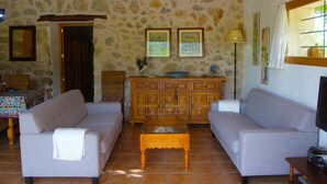 Una sala de estar con dos sofás, una mesa de centro y una pared de piedra. Hay un aparador de madera y un televisor sobre un pedestal.