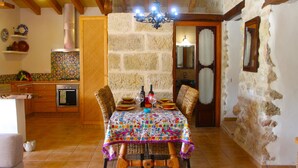 Comedor con una mesa dispuesta para cuatro personas, sillas de mimbre, mantel estampado y pared de piedra.