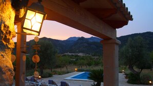 Un espacio exterior techado con piscina, sillas de descanso y vistas a las montañas.