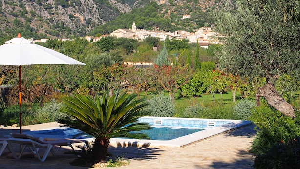 Zona de piscina con sillas de descanso y una sombrilla, rodeada de vegetación y montañas al fondo.