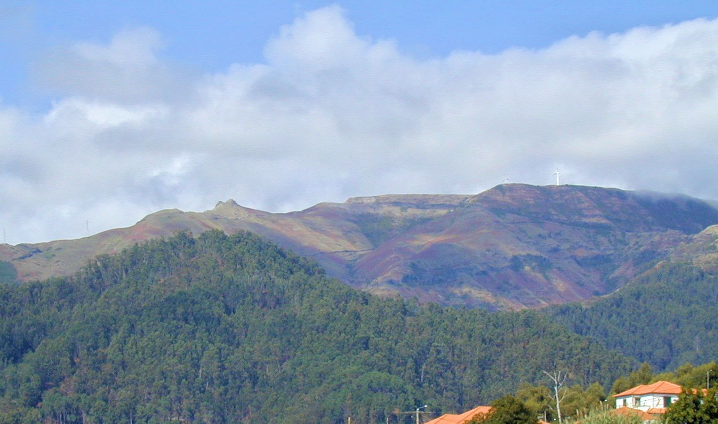 Un paysage montagneux avec une colline bois ée et une éolienne visible au loin.