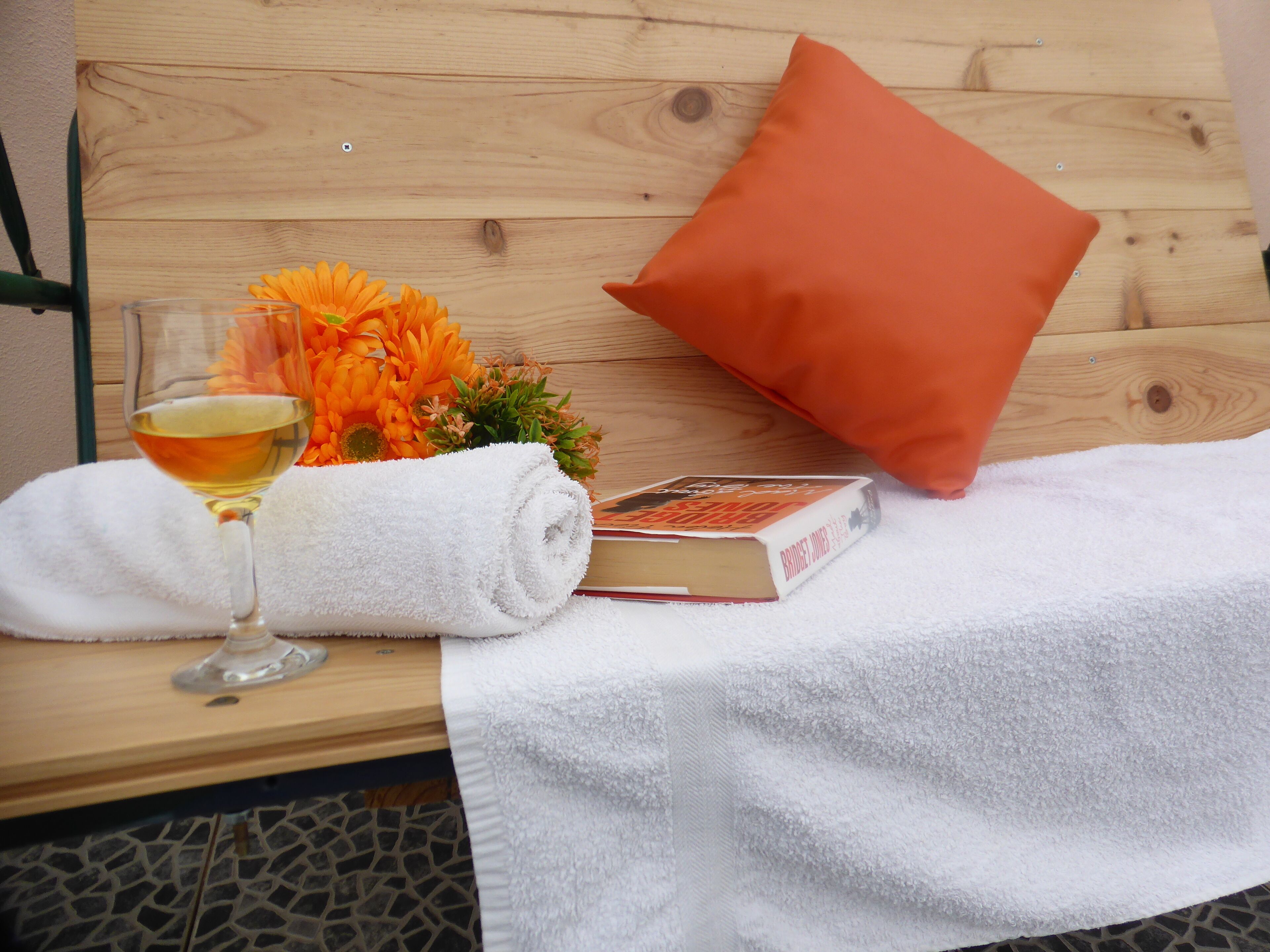 Un banc en bois, une serviette blanche, un verre de vin, un livre et un bouquet de fleurs.