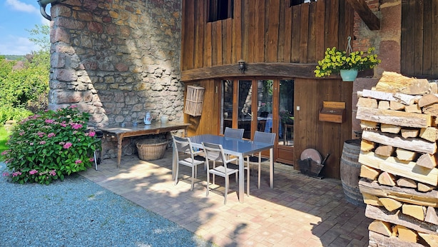 A rustic stone building with a wooden balcony, outdoor seating, and a stone wall.