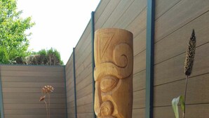 A wooden sculpture in a garden area with gravel, a wooden fence, and some plants.