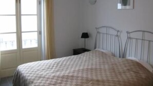 A bedroom with a bed, a nightstand, a lamp, a window with curtains, and a wall-mounted picture. - Spacious apartment in restored manor house on Tavira riverfront (WiFi) (Tavira)