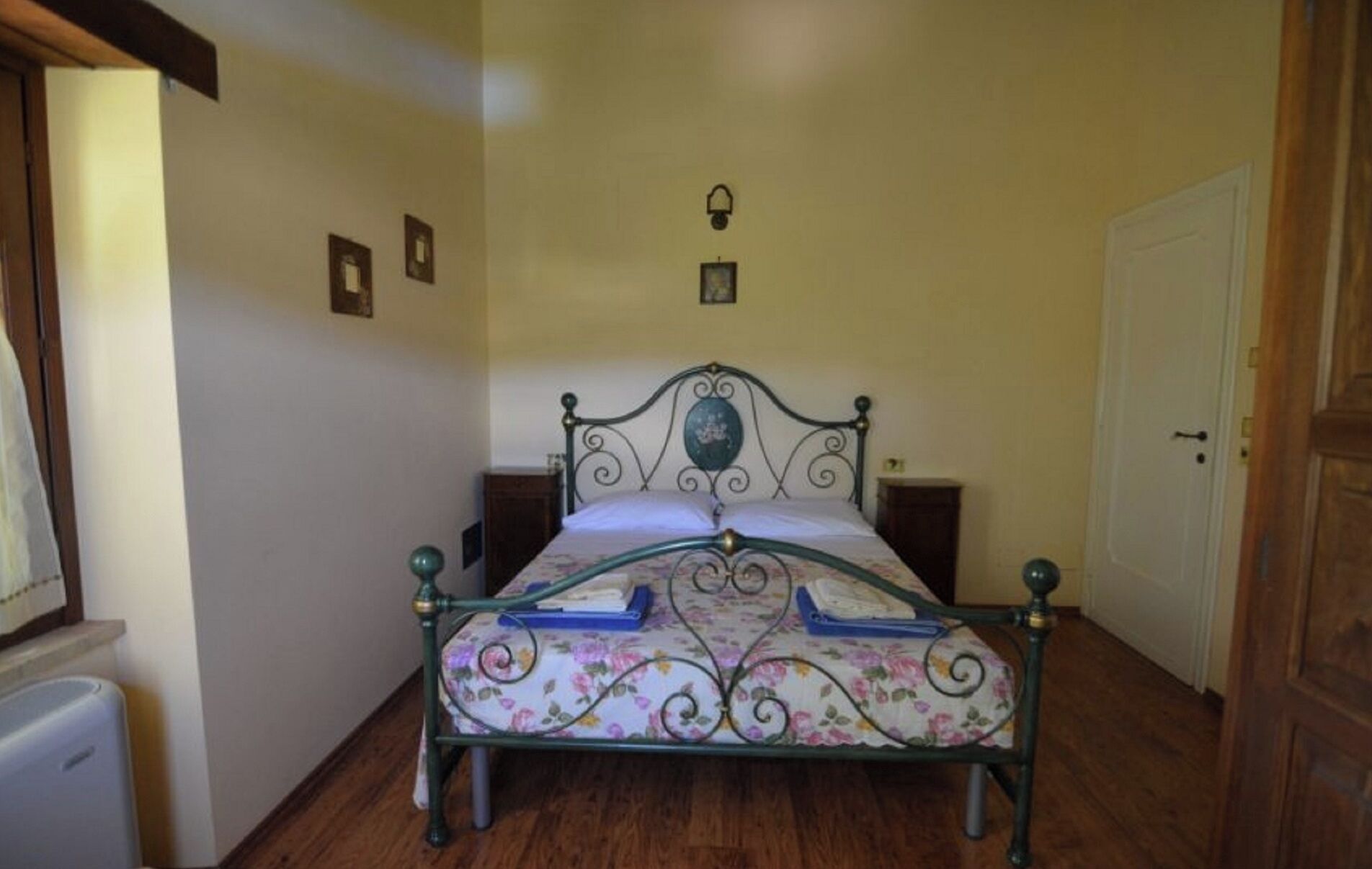 A bedroom with a bed, wooden floor, a door, and a small cabinet.