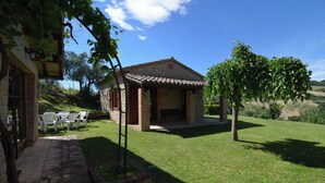 A rustic stone house with a tiled roof, a small patio with chairs, and a lawn. - Charming Villa in Marche, private pool and fantastic landscape (Gauldo, Macerata)