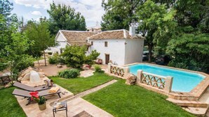 A backyard with a swimming pool, a patio with a table and chairs, and a small white house with a tiled roof. - Casa rural La Alameda for 6 people (Madridejos)
