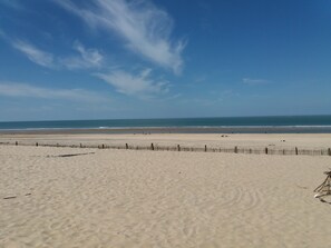 A wide sandy beach with a wooden fence in the foreground and a clear blue sky. - Villa Soulacaise seaside (Soulac-Sur-Mer)