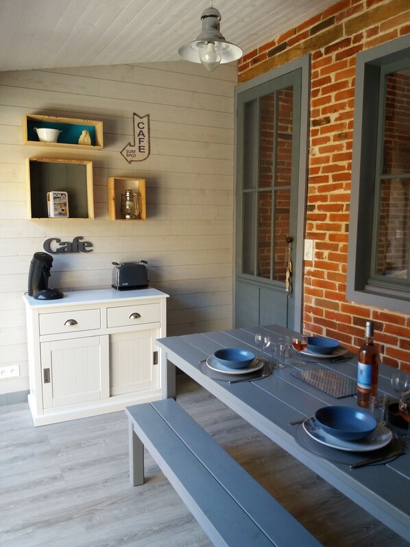A kitchen with a long table, white cabinets, and a brick wall. - Villa Soulacaise seaside (Soulac-Sur-Mer)