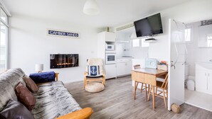Una sala de estar moderna con un sofá, una silla de madera, una mesa de comedor y una cocina con armarios blancos y un televisor.