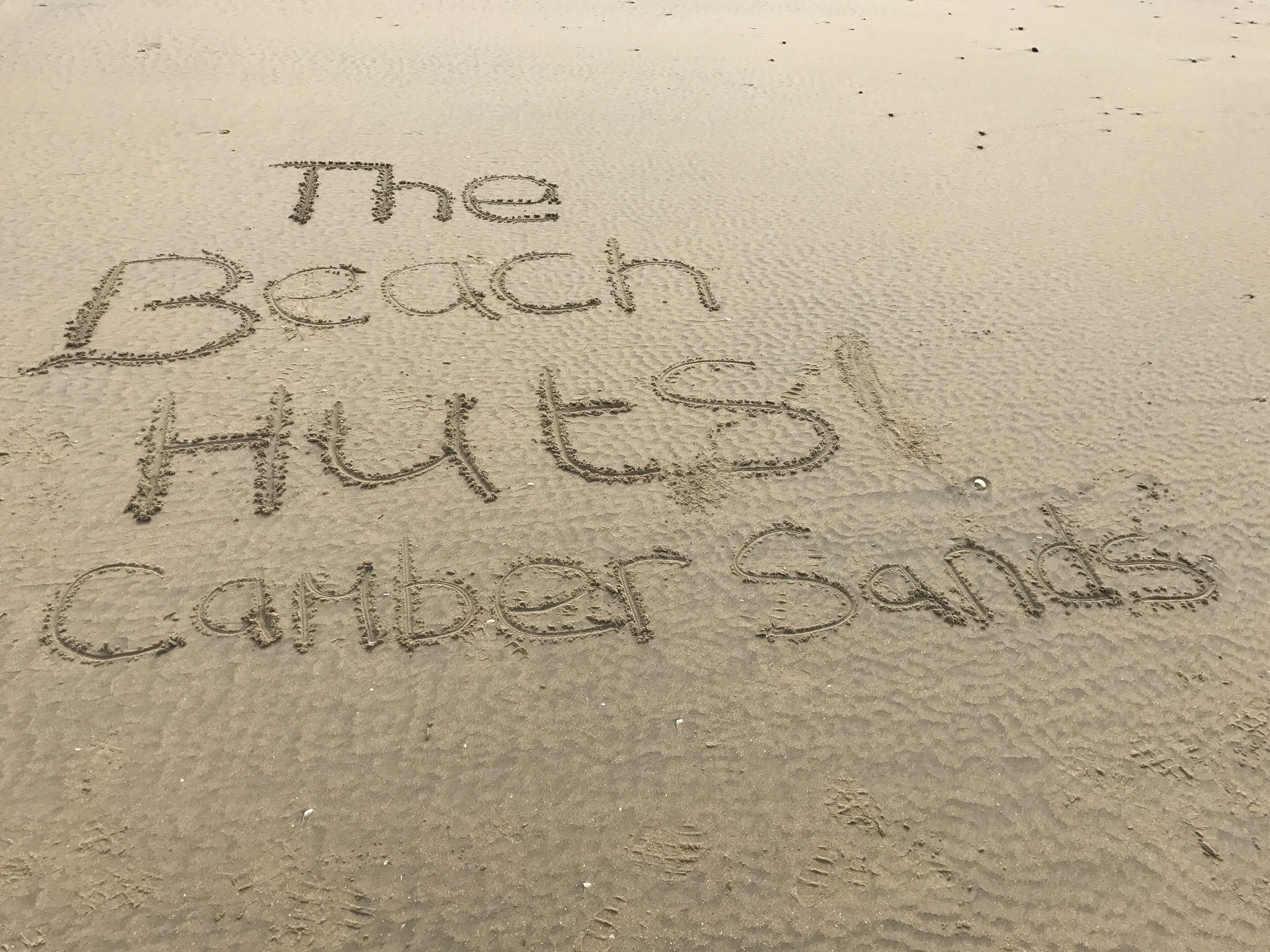 La scritta "The Beach Huts" incisa sulla sabbia.