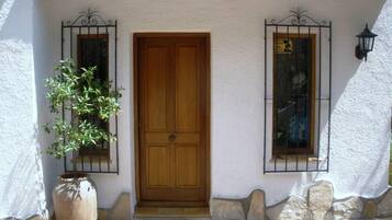A wooden door with a white stucco wall, a potted plant, and two windows with metal grilles.