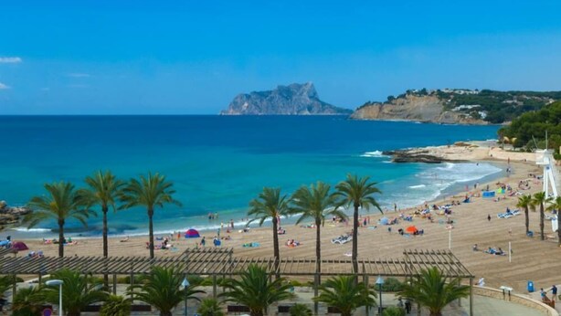 A beach with palm trees, a clear blue sky, and a rocky outcrop in the distance. - House / Villa - MORAIRA (Moraira)