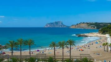 A beach with palm trees, a clear blue sky, and a rocky outcrop in the distance.