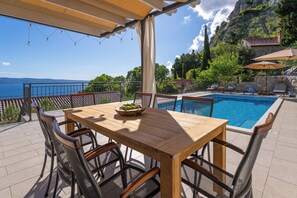 Eine Terrassenanlage im Freien mit Holztisch und -stühlen, einem Schwimmbecken und Blick auf das Meer.