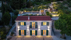 Un bâtiment en pierre avec un toit recouvert de tuiles rouges, des volets verts et un balcon doté de sièges pour l’extérieur.