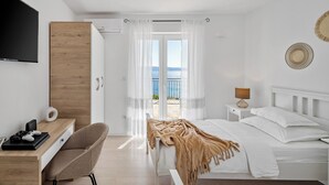 Une chambre d’hôtel avec un lit, un bureau et une chaise, une télévision et une vue sur la mer.