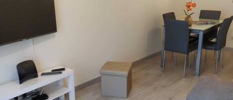 Een moderne woonkamer met een flatscreen televisie, een eettafel met stoelen, een klein voetenbankje en een bank.