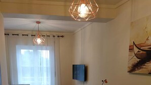 Una sala de estar moderna con un sofá, una mesa de comedor con sillas, un televisor montado en la pared y un cuadro.