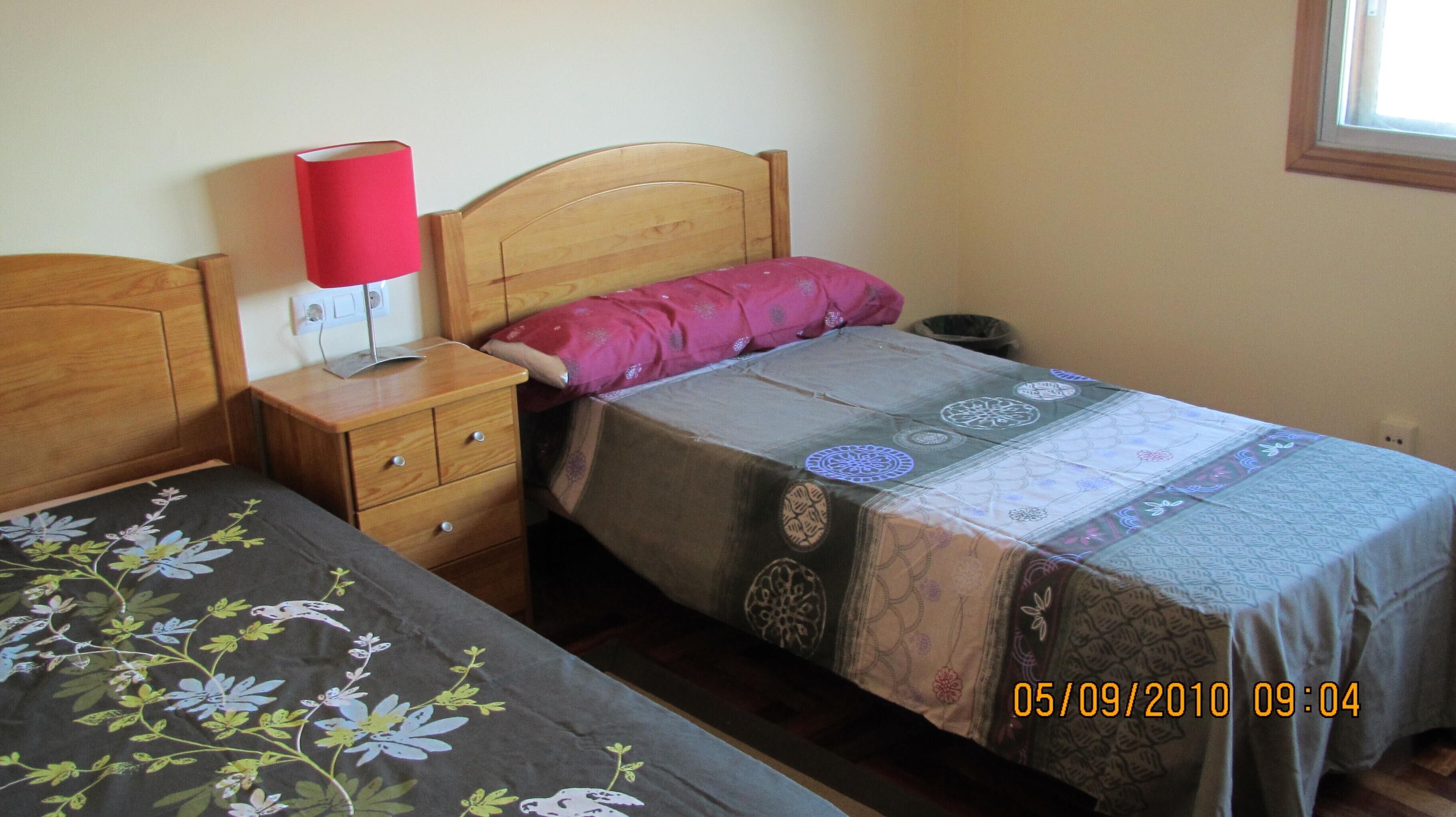 Quarto com duas camas de solteiro, uma mesa de cabeceira com abajur e uma janela.