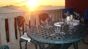 A round metal table set for dining with chairs, glasses, and plates, overlooking a sunset. - Luxury Villa with private pool, amazing ocean views, 100m to sandy beach, Wi Fi (Vigo)
