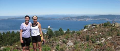 Two people standing on a rocky hillside with a view of a coastal city and the ocean in the background.