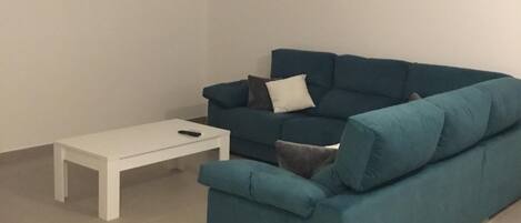 Una sala moderna con un sofá azul, una mesa de centro blanca y un proyector instalado en el techo.